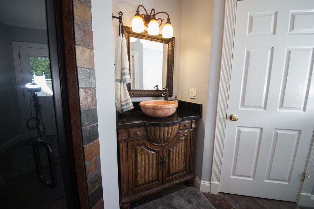 Bathroom with ornate wooden vanity, stone sink, black countertop, mirror, and light fixture. White door on the right.