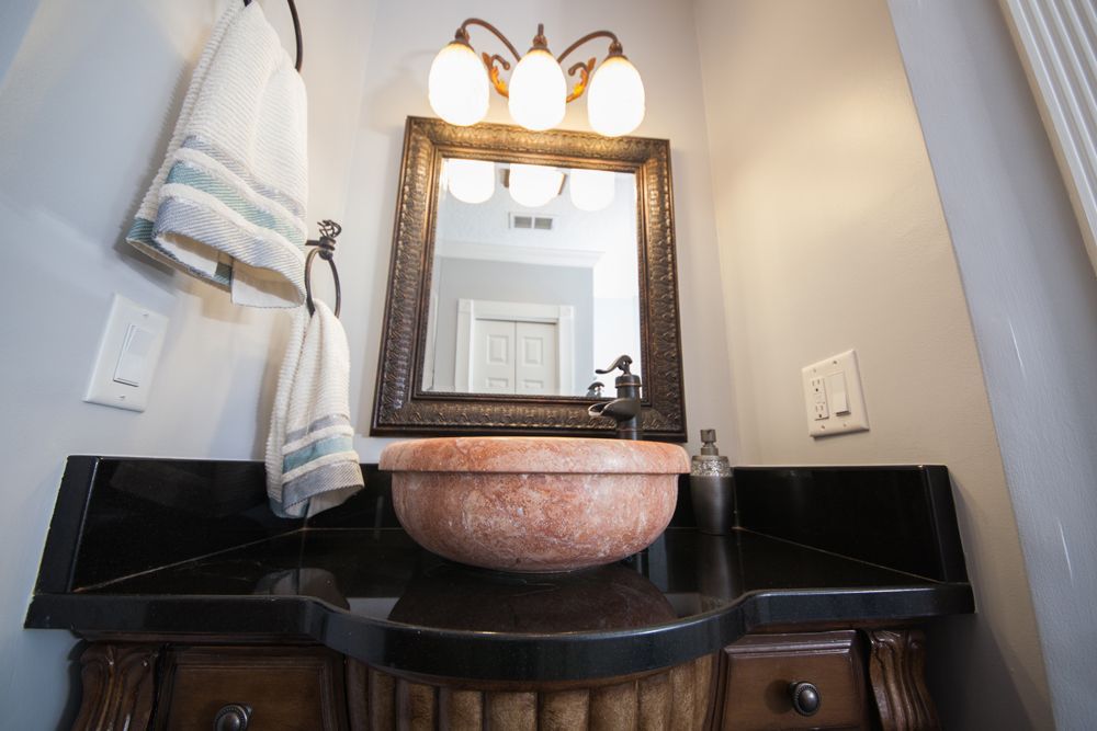 Bathroom vanity with a rose-colored basin, ornate mirror, and dark countertop. Towels hang to the left.
