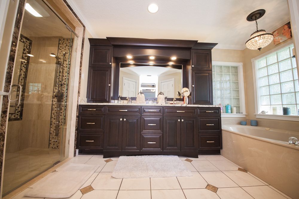 Dark wood bathroom vanity with a large mirror, cabinets, and a shower, with a tub and window.