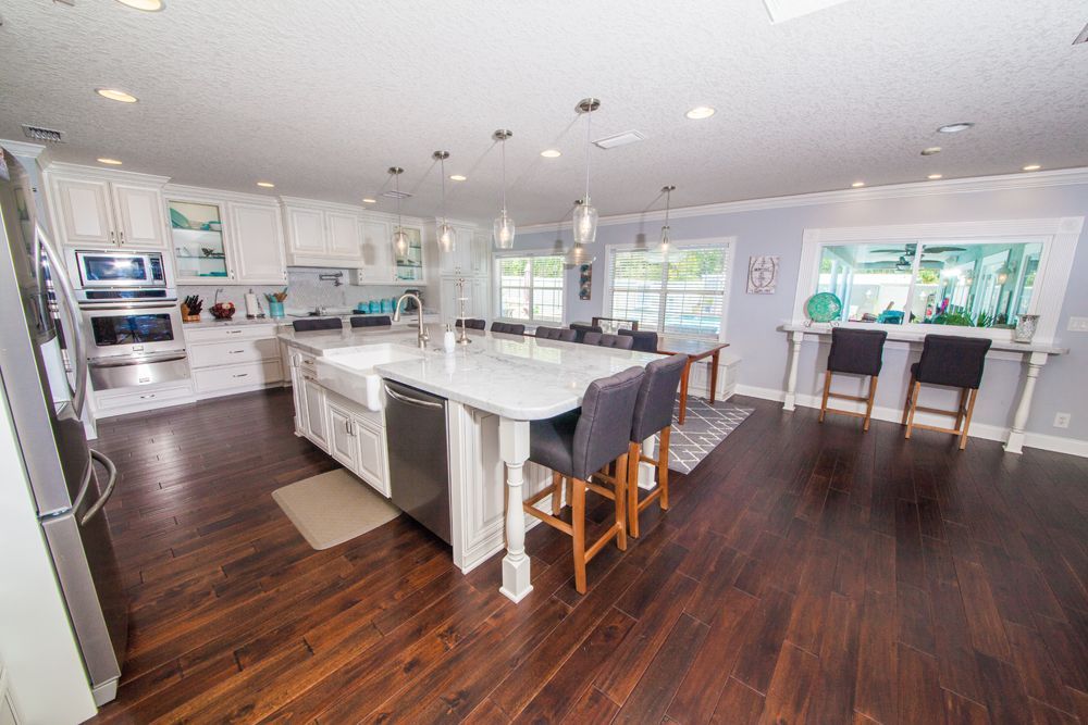 Spacious kitchen with white cabinets, large island, dark wood floors, and a dining area.