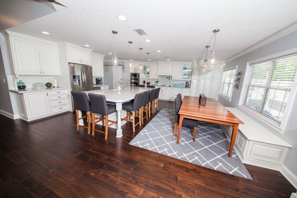 Spacious modern kitchen with white cabinets, island with bar stools, dining table, and hardwood floors.
