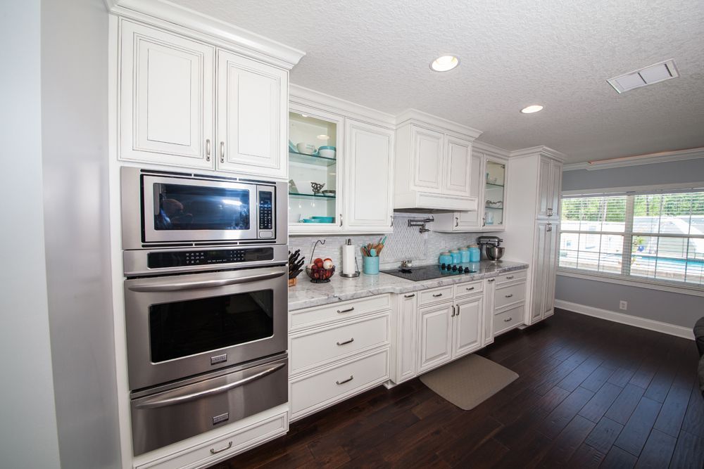 White kitchen with stainless steel appliances, white cabinets, marble countertops, and dark wood floors.