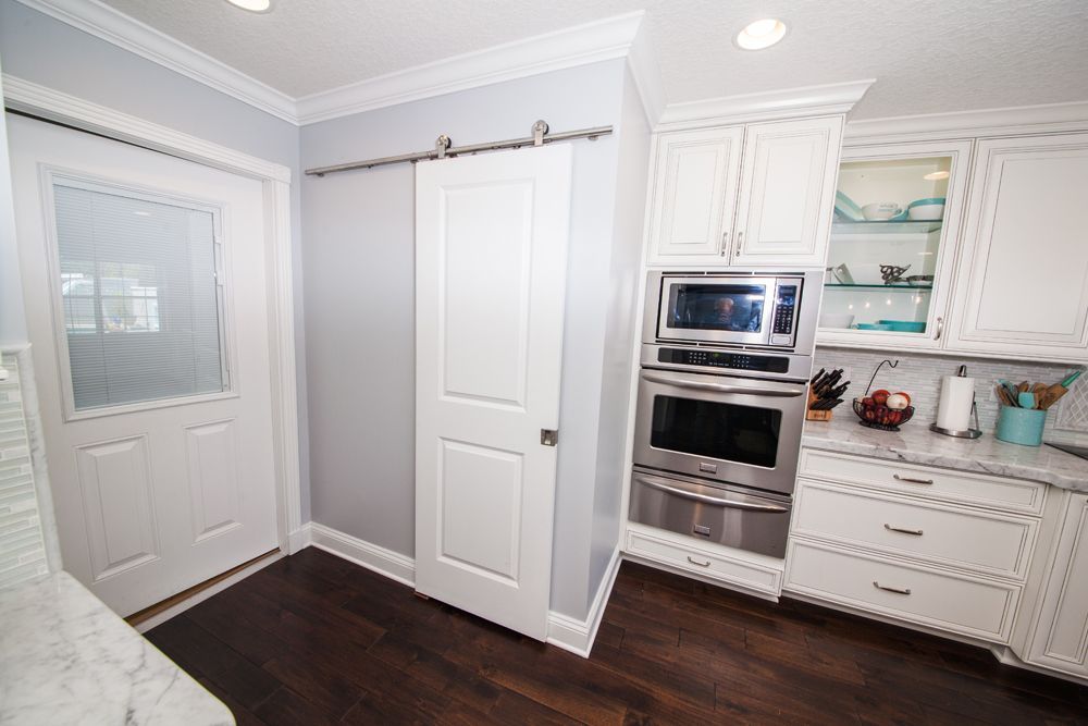 White kitchen with dark wood floor, a sliding door, and built-in oven and microwave.
