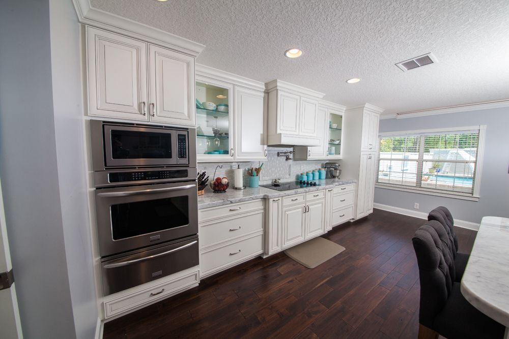 White kitchen with stainless steel appliances and dark wood floors.