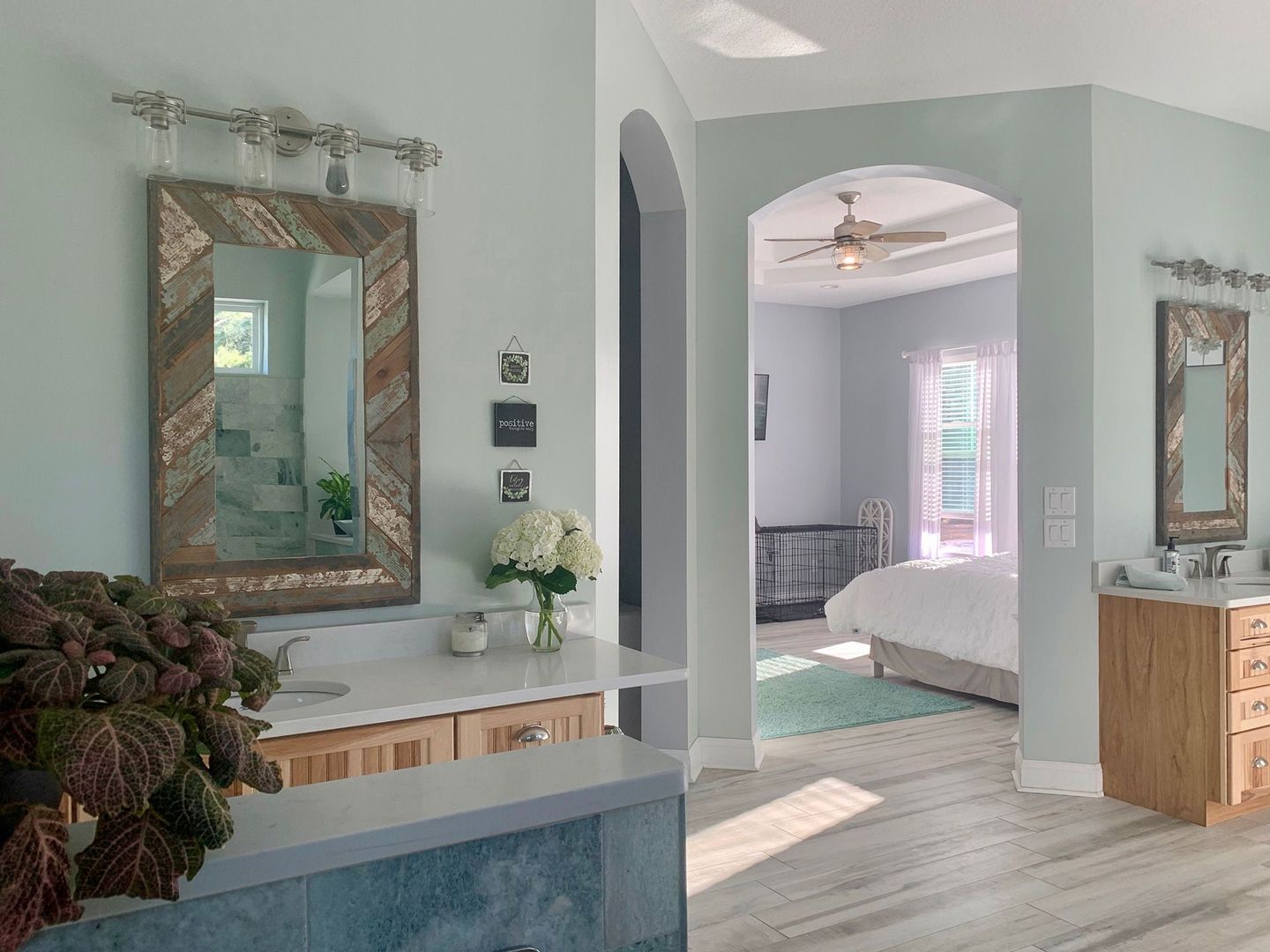 A light blue-painted master bathroom with a vanity, mirror, and archway leading to the bedroom.