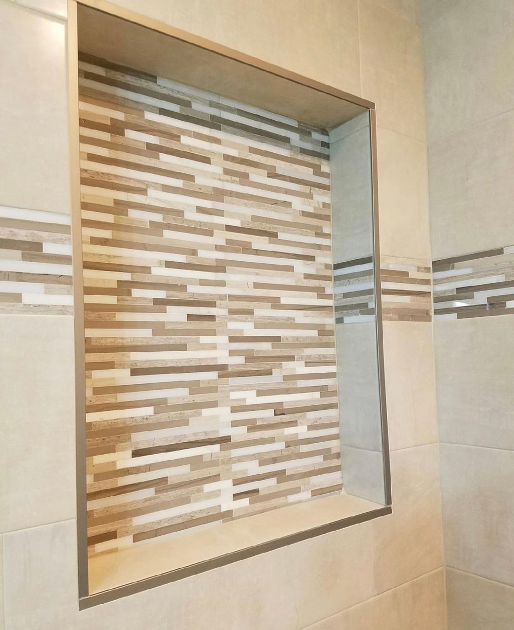 Recessed shower shelf with tan and wood-toned tile, framed by silver trim in a bathroom.