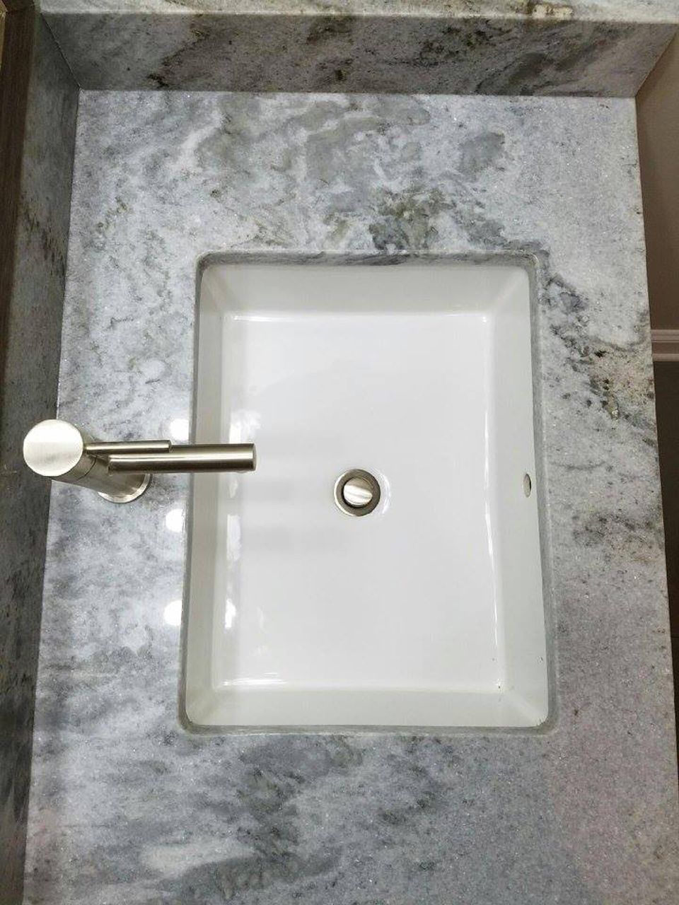 White rectangular bathroom sink inset in a gray granite countertop; stainless steel towel bar on the left.