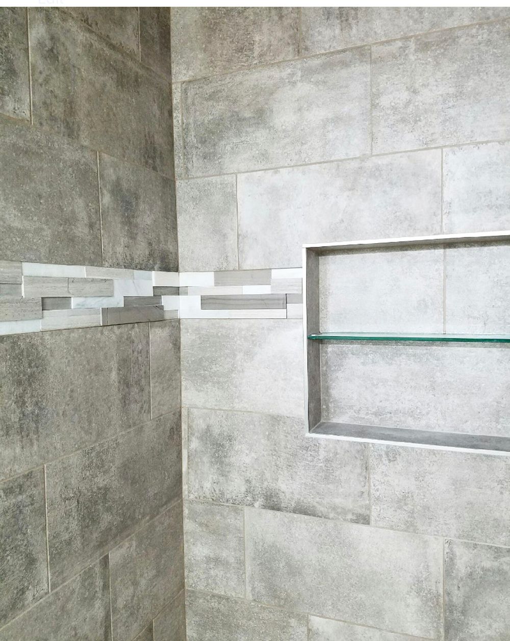 Gray tiled shower with a shelf and accent strip.