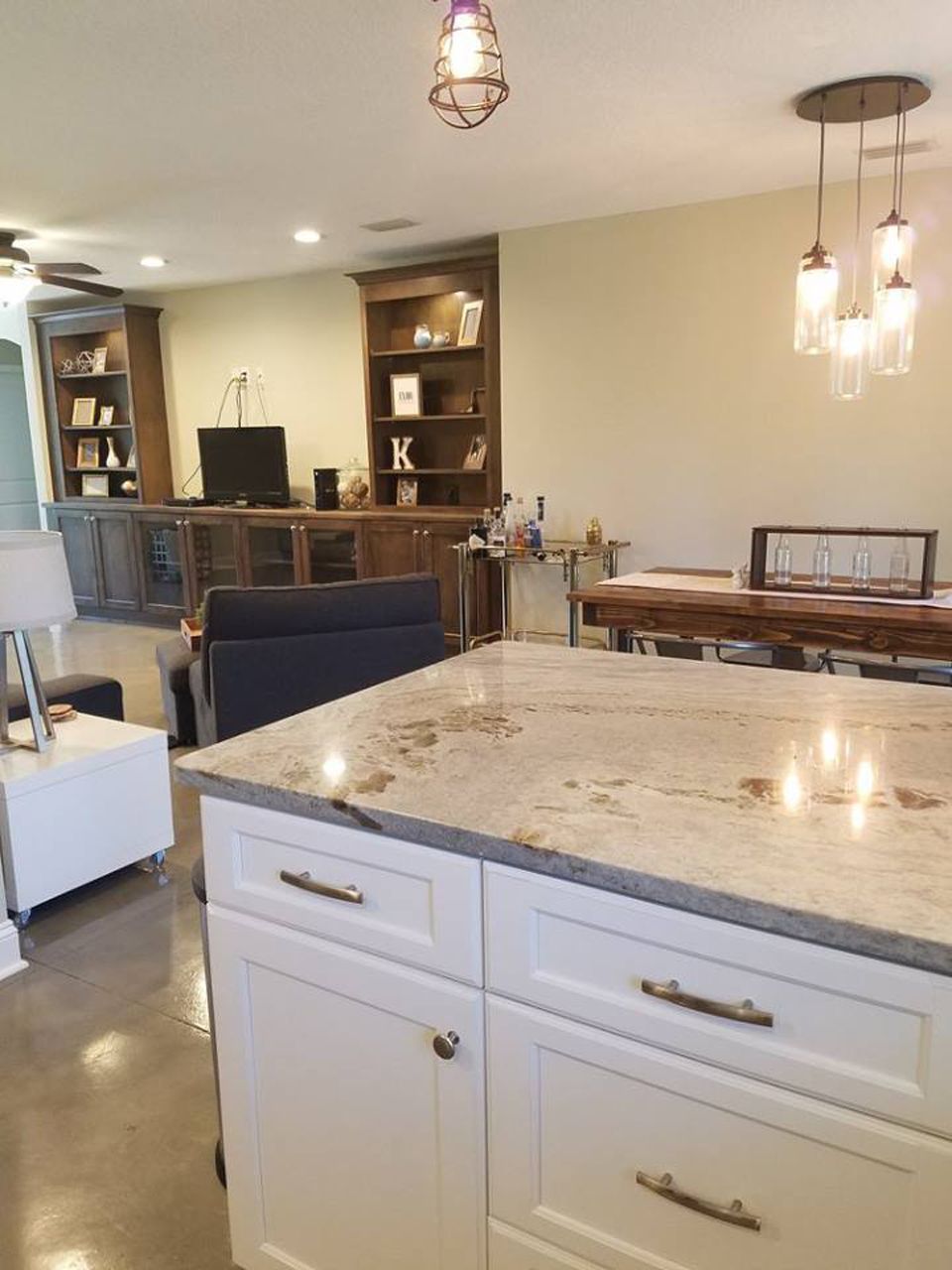Kitchen island with granite countertop, white cabinets, and open living space with dark wood built-ins and dining table.