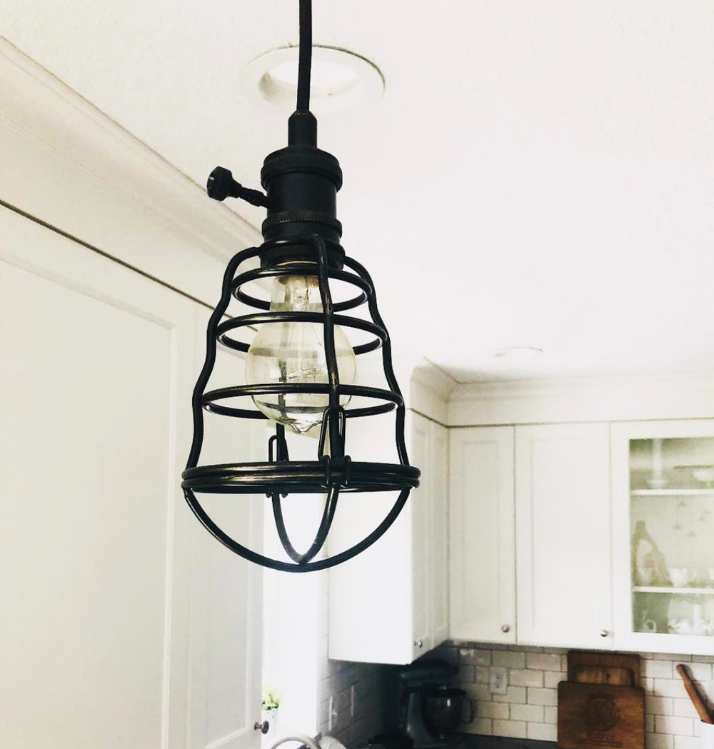 Black caged pendant light in a white kitchen with white cabinets.