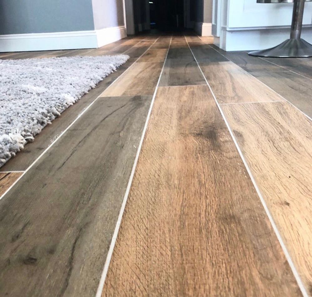 Wood-look tile floor in a hallway, with a rug on the left and a glimpse of a dark room ahead.