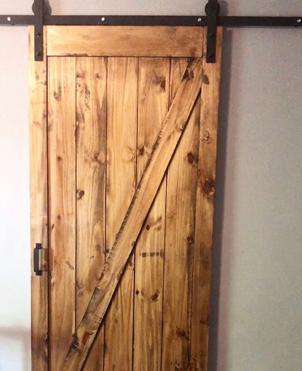 Wooden barn door with diagonal support, hanging on black hardware.