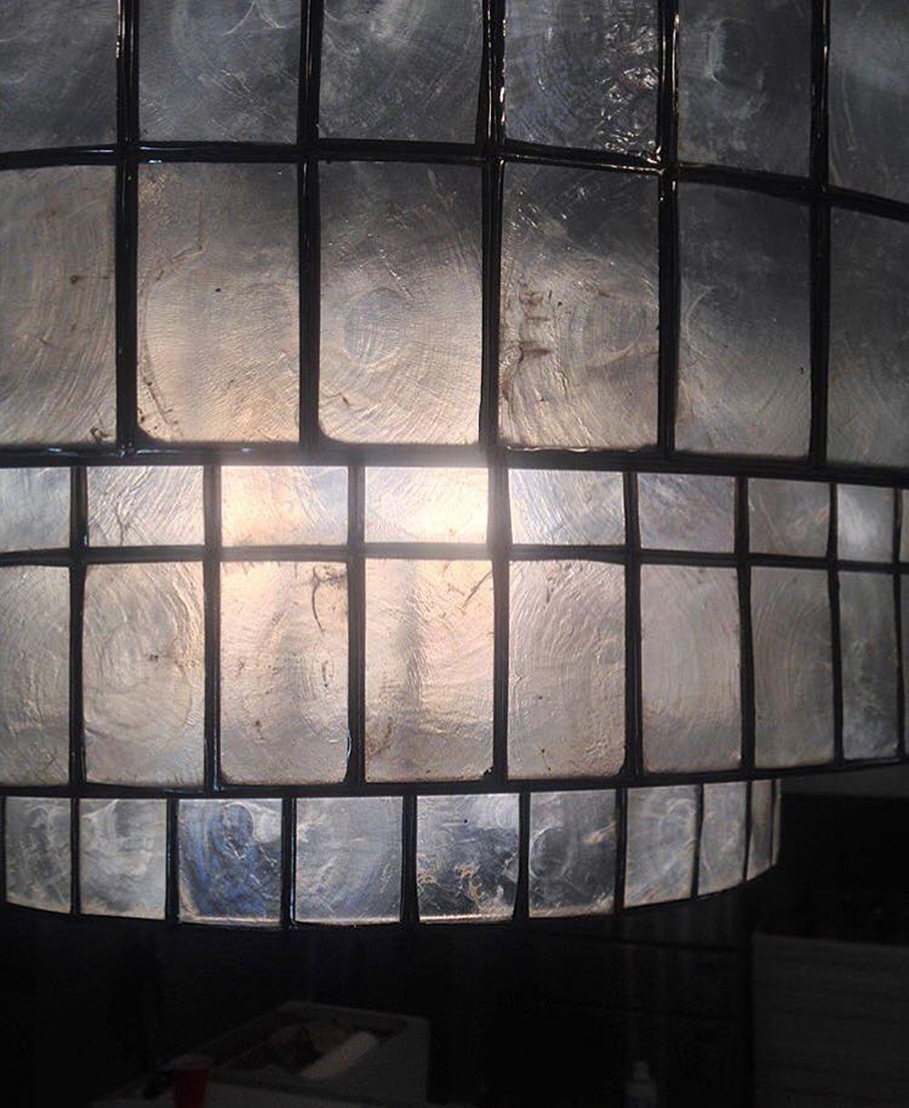 Close-up of a layered, textured lamp shade with a grid of translucent, square panels, illuminated from within.