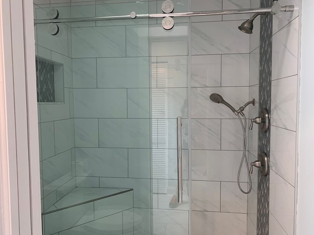 Glass shower with white tile walls, silver fixtures, and a built-in bench.