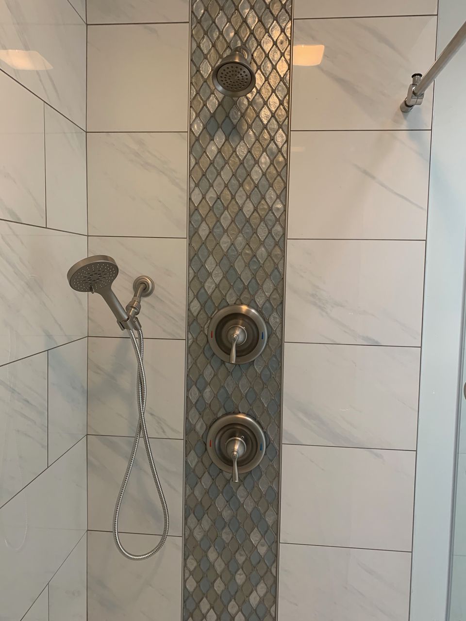 Shower with white marble-like tiles, mosaic accent strip, and multiple showerheads.