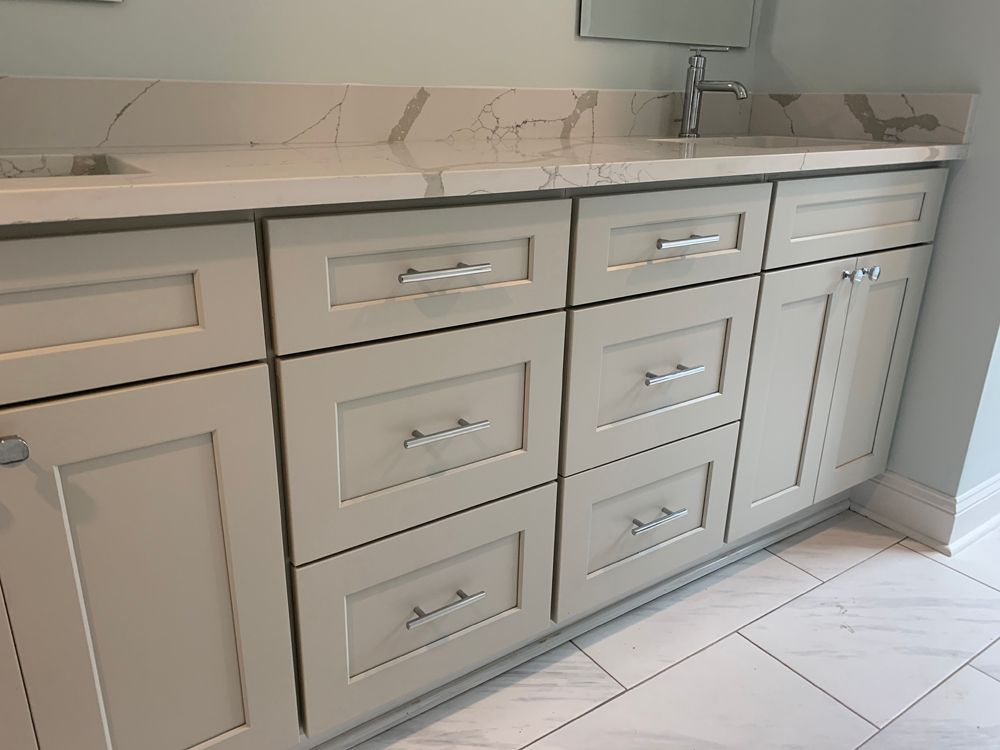 Light gray bathroom vanity with drawers and cabinets, silver hardware, and marble countertop.