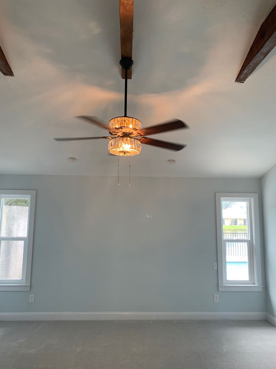 Bedroom with a crystal chandelier ceiling fan, two windows, and light blue walls.