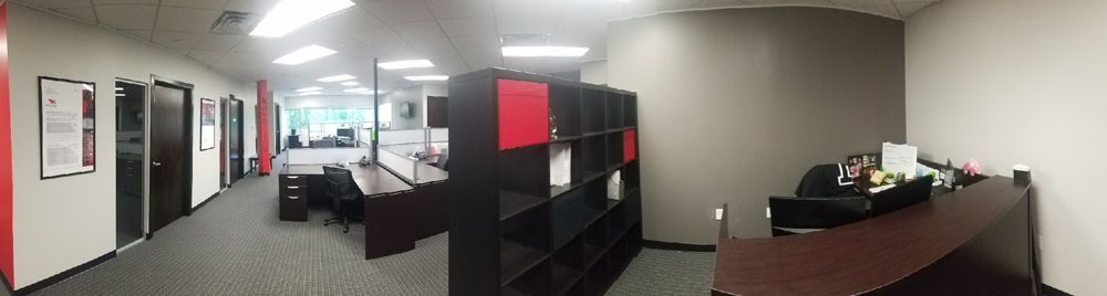 An office interior with desks, shelves, doors, and a reception desk. Red and black accents are present.