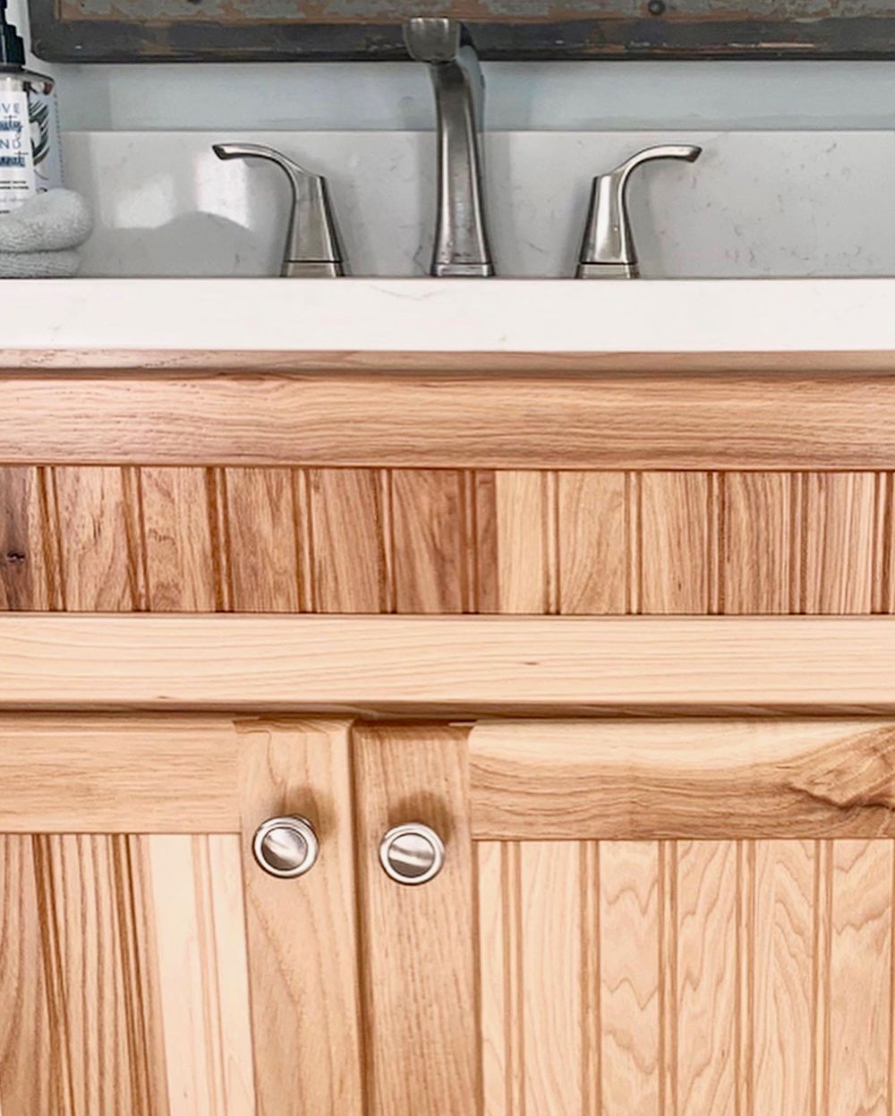 Wooden bathroom vanity with a white countertop and silver faucet.