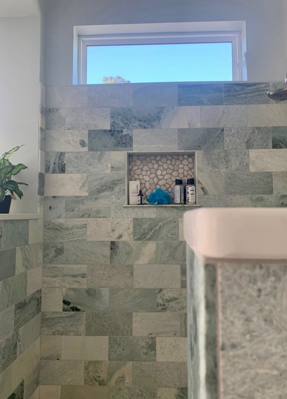 Shower with green and white tiled walls, a window, and a built-in shelf holding toiletries.