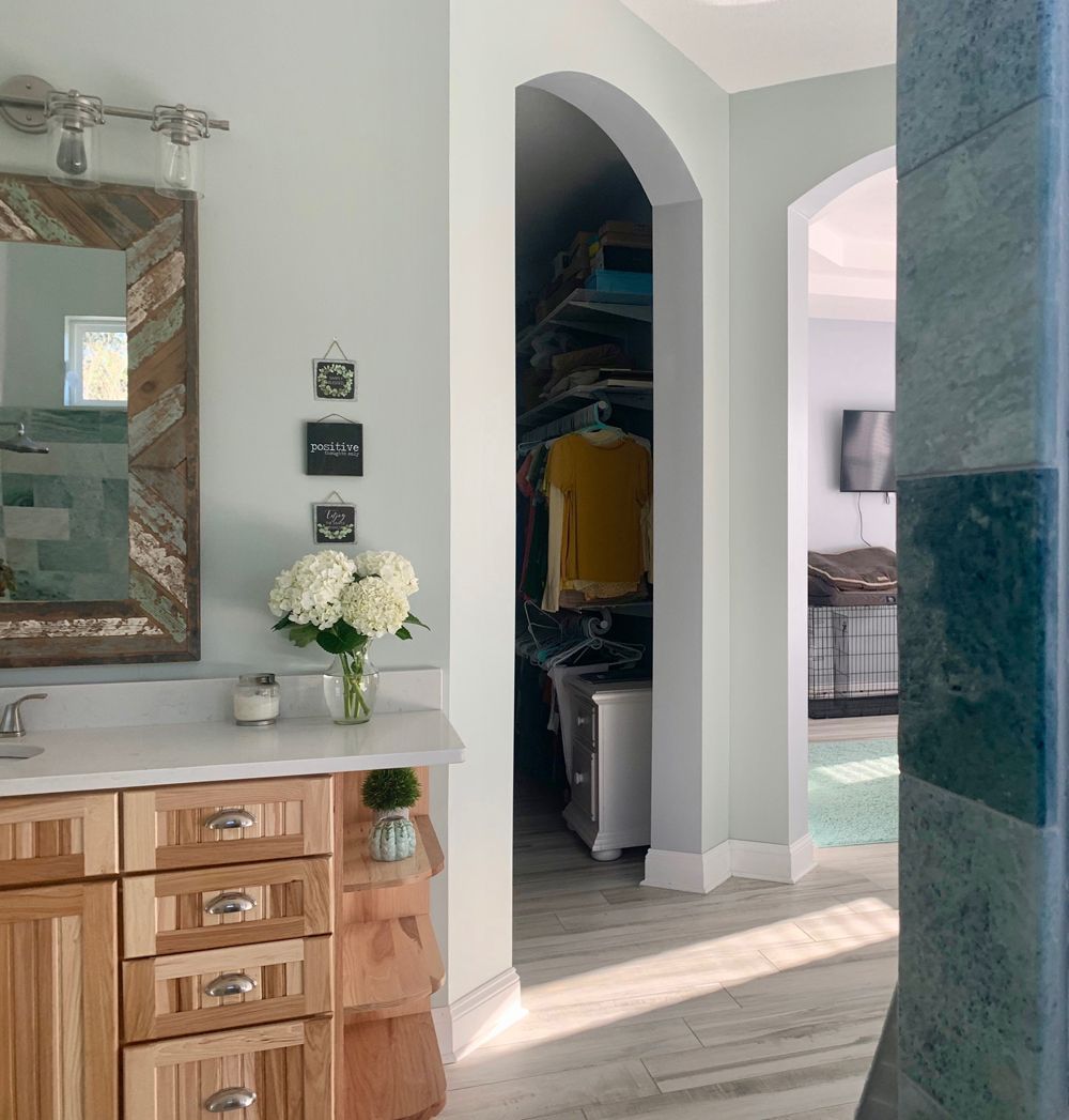 Bathroom with light blue walls, wooden vanity, and an arched doorway leading to a closet.