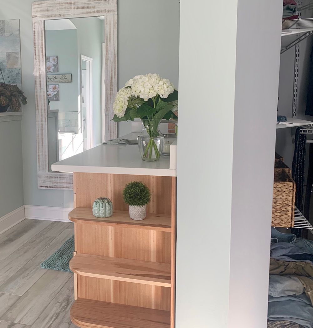 A light-filled room with a wooden bar and shelving, a large mirror, and flowers.