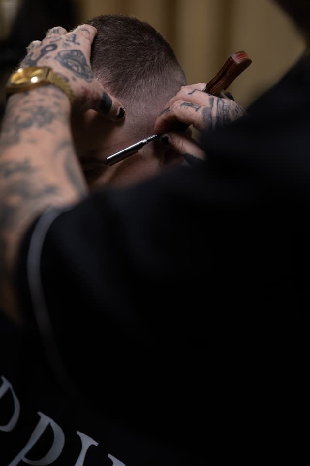 Barber trimming a client’s hair with clippers, close-up with tattooed hands.