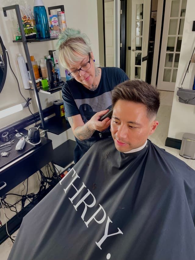 Hairdresser trimming a man’s hair in a salon, with cape and styling tools visible