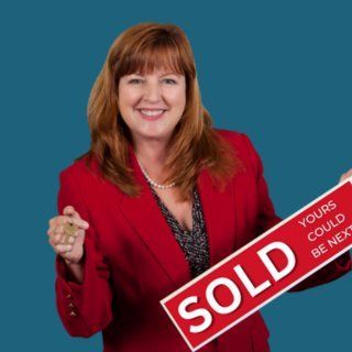 Cheryl Coleman Smiling woman in red blazer holding a large SOLD sign on a blue background