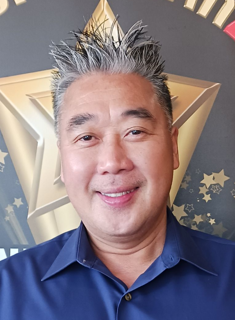 Dennis K. Ng Smiling man with spiky gray hair, wearing a blue shirt, in front of a golden star.
