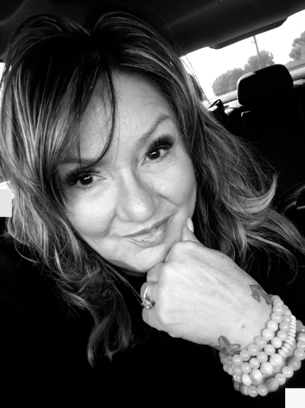 Kat Donahue Black-and-white selfie of a smiling person resting their chin on a hand in a car