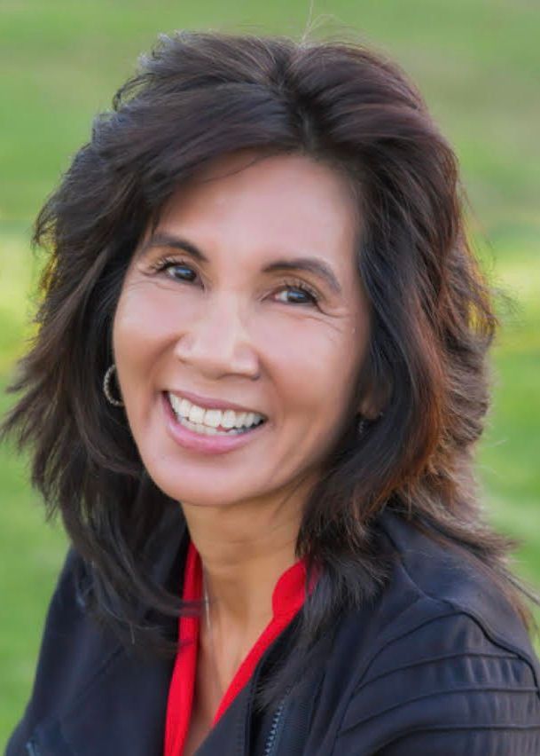 Dr. Lisa Owyang Anton Woman with dark hair smiles broadly; wears a black jacket over a red top, outdoors.