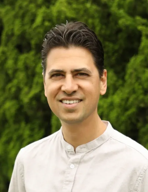 Mukunda Singh Smiling man in a white shirt standing outdoors in front of green trees