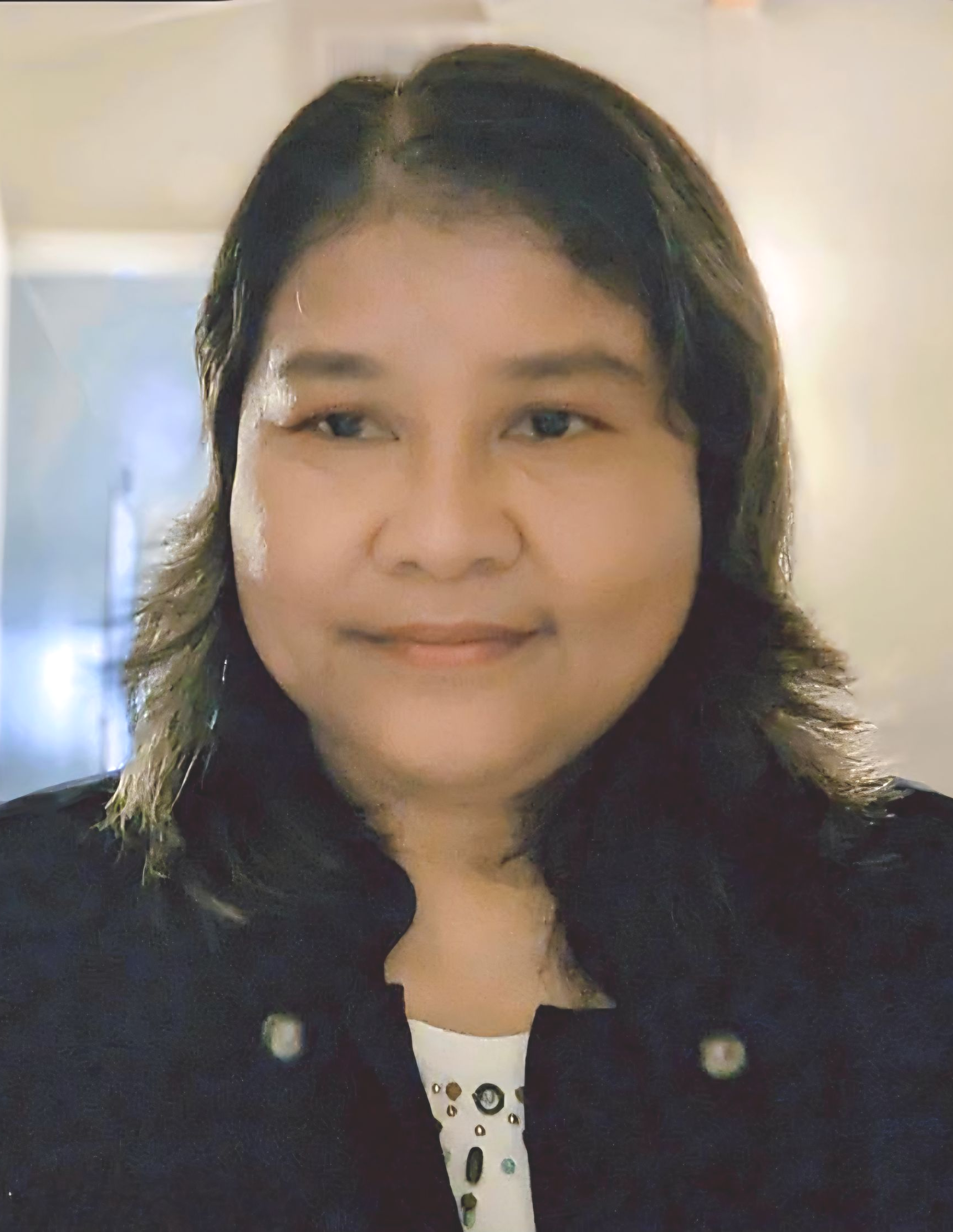 Theeraporn Portrait of a woman smiling softly, wearing a dark jacket against a blurred indoor background