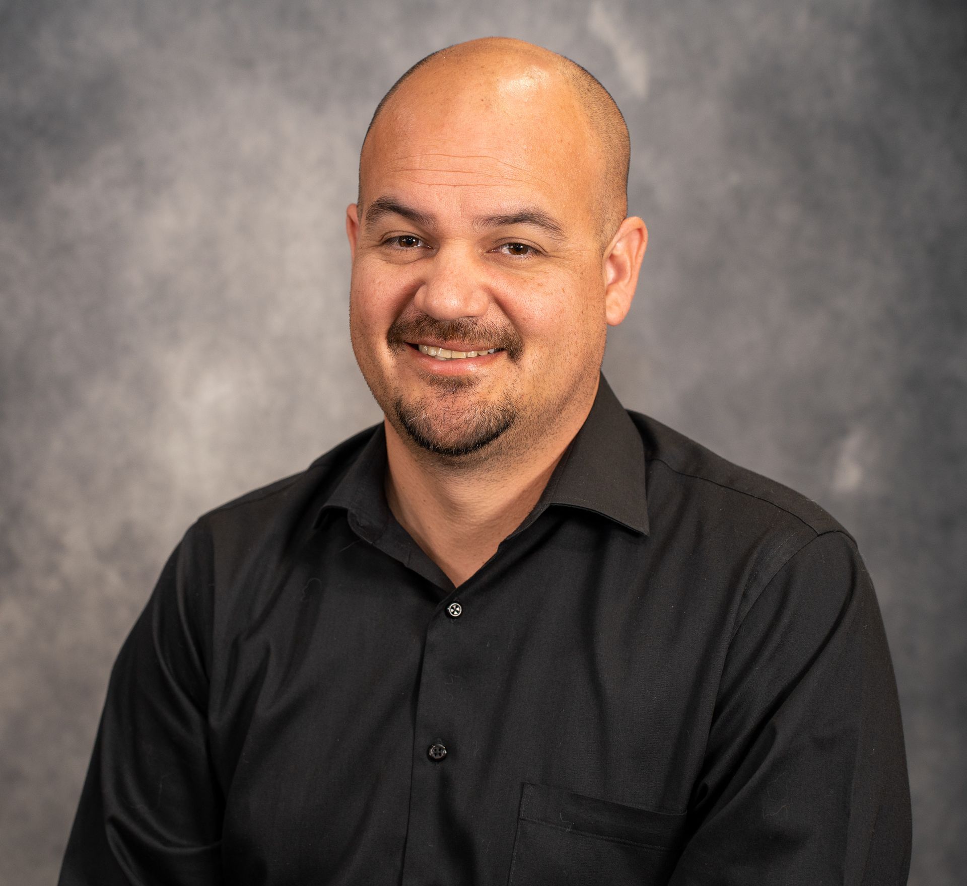 Victor Burke Portrait of a smiling bald man in a black shirt against a gray studio backdrop