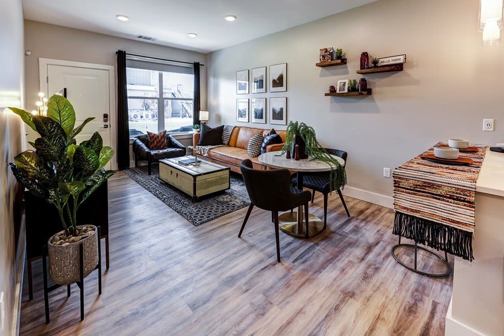 Modern living room with gray sofa, plants, dining table, wall art, and wood-look flooring at Icon Apartment Homes at Ferguson Farm, offering apartments in Bozeman, MT.