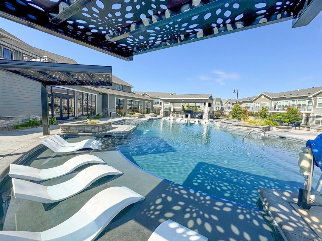 A large swimming pool with lounge chairs and a building in the background at Icon Apartment Homes at Ferguson Farm in Bozeman, MT.