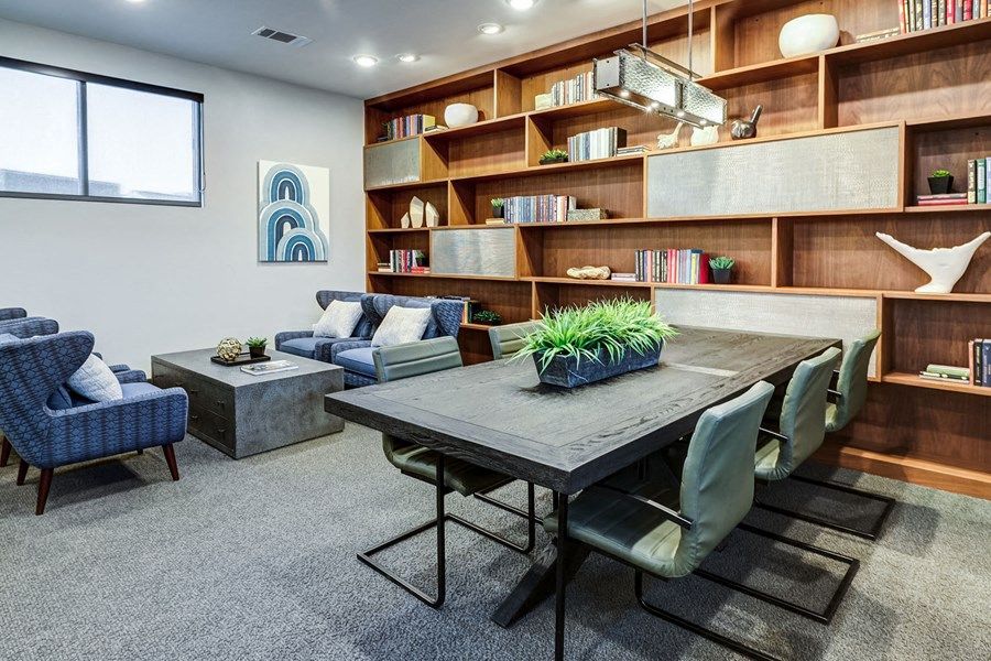 Modern lounge with blue chairs, gray sofas, a long wooden shelf wall, and a dark table with chairs at Icon Apartment Homes at Ferguson Farm in Bozeman, MT.