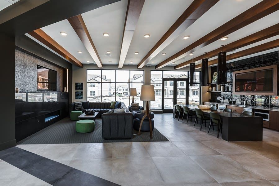 Modern lounge with wood-beam ceiling, seating area, bar, and large windows overlooking outdoors at Icon Apartment Homes at Ferguson Farm in Bozeman, MT.