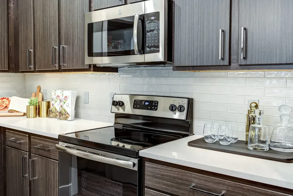 Modern kitchen with stainless steel microwave and oven, dark cabinets, white countertops, and white tile backsplash at Icon Apartment Homes at Ferguson Farm, offering apartments in Bozeman, MT.