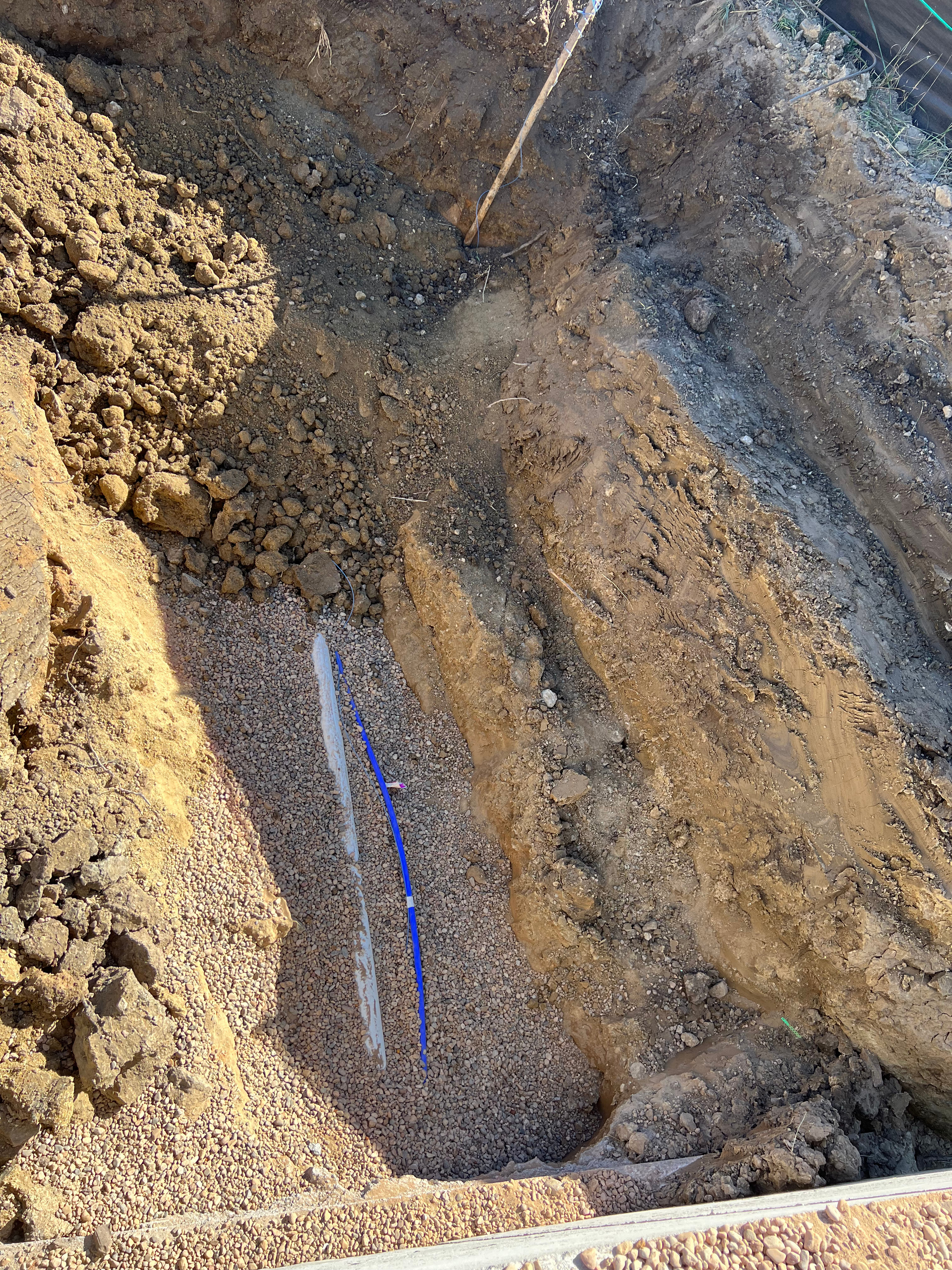 A blue pipe is laying in the dirt in a hole.
