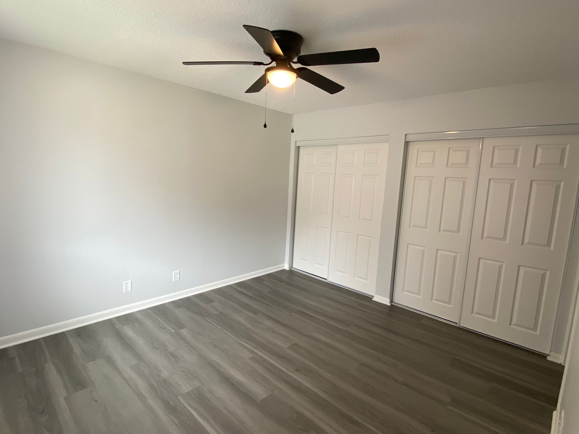 Empty carpeted room with white walls, three windows, and a ceiling fan with light on.