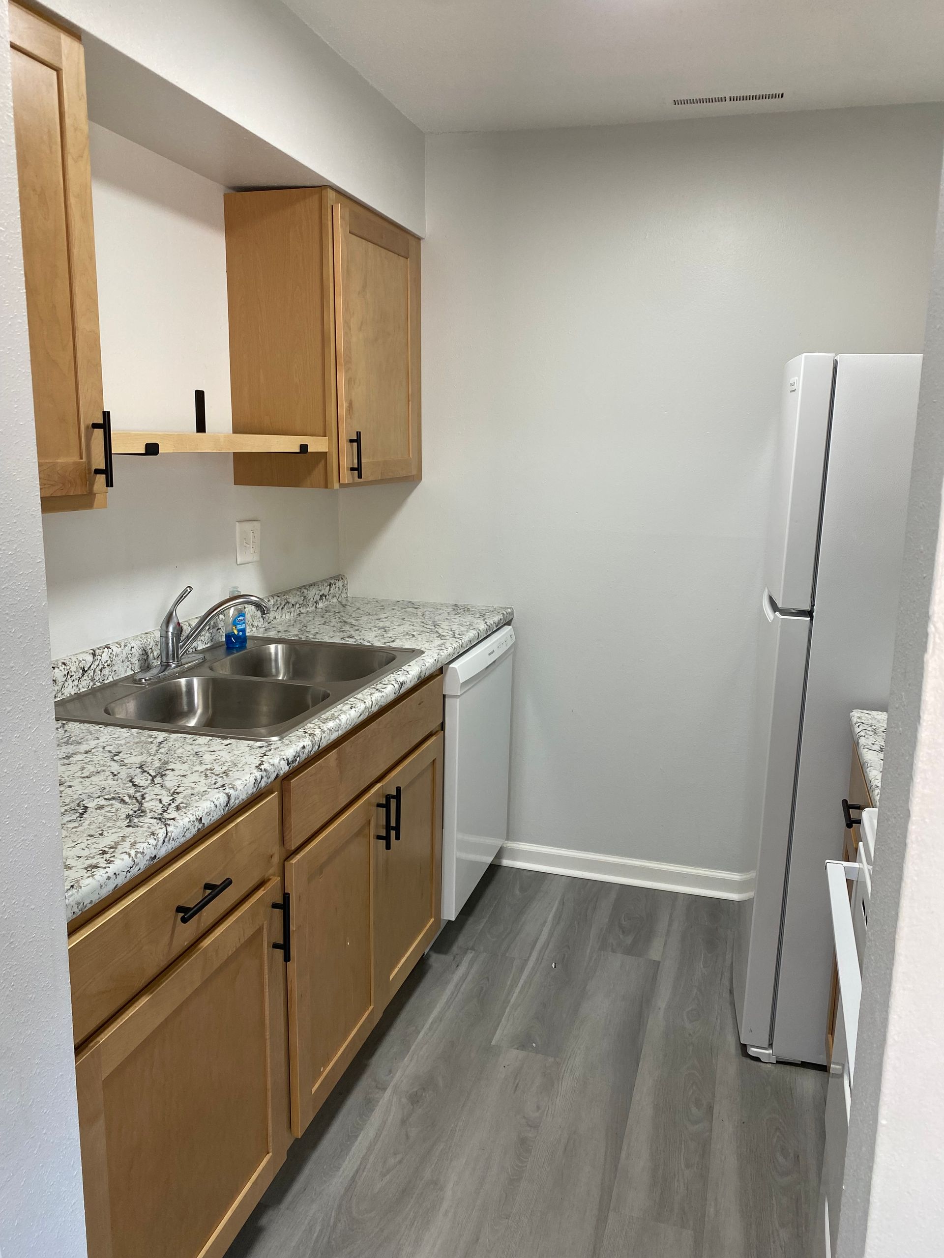 Narrow galley kitchen with white cabinets, gray floor, stove, sink, refrigerator, and overhead light.