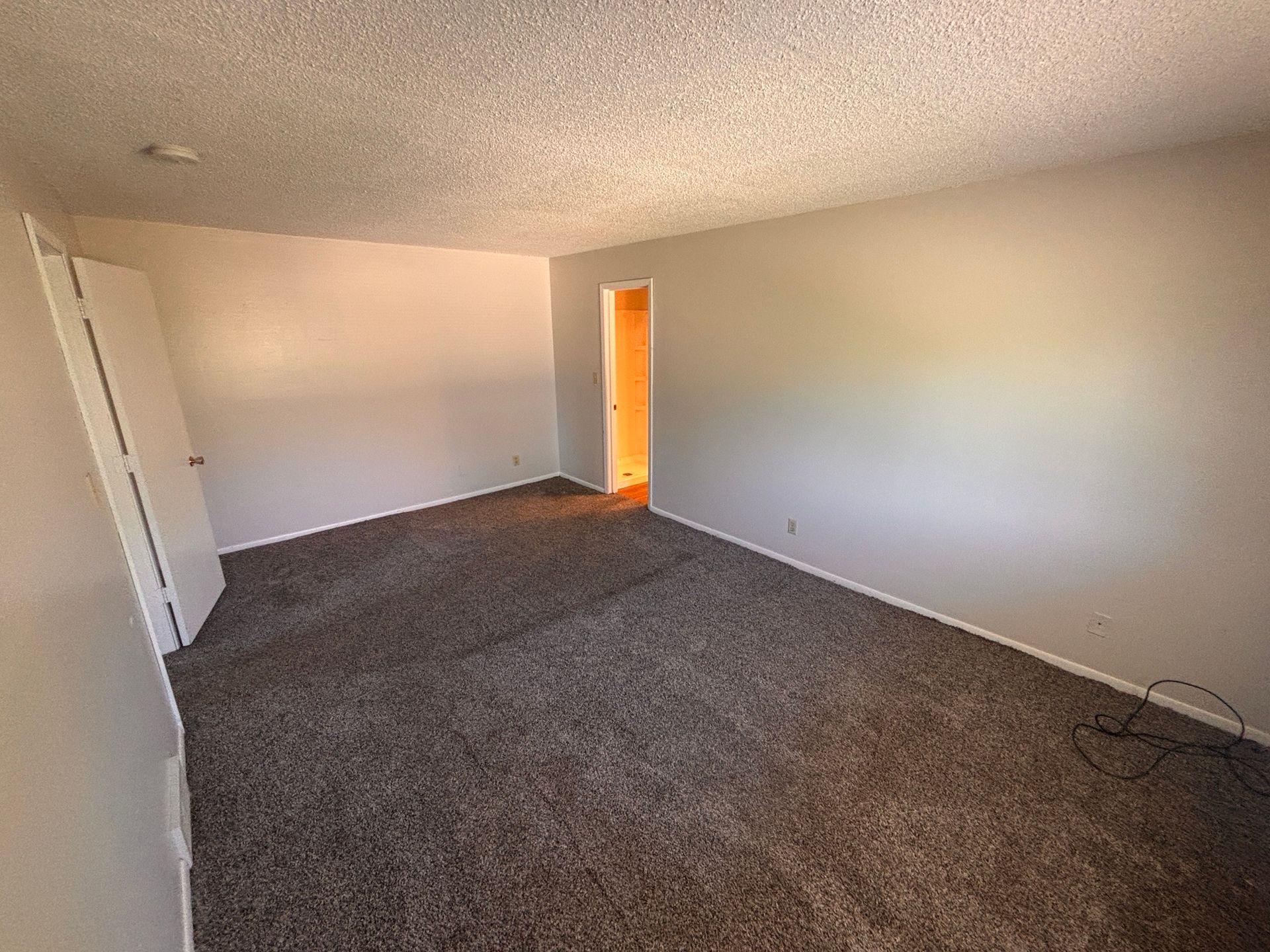 Empty carpeted living room with beige walls and an open orange-lit doorway