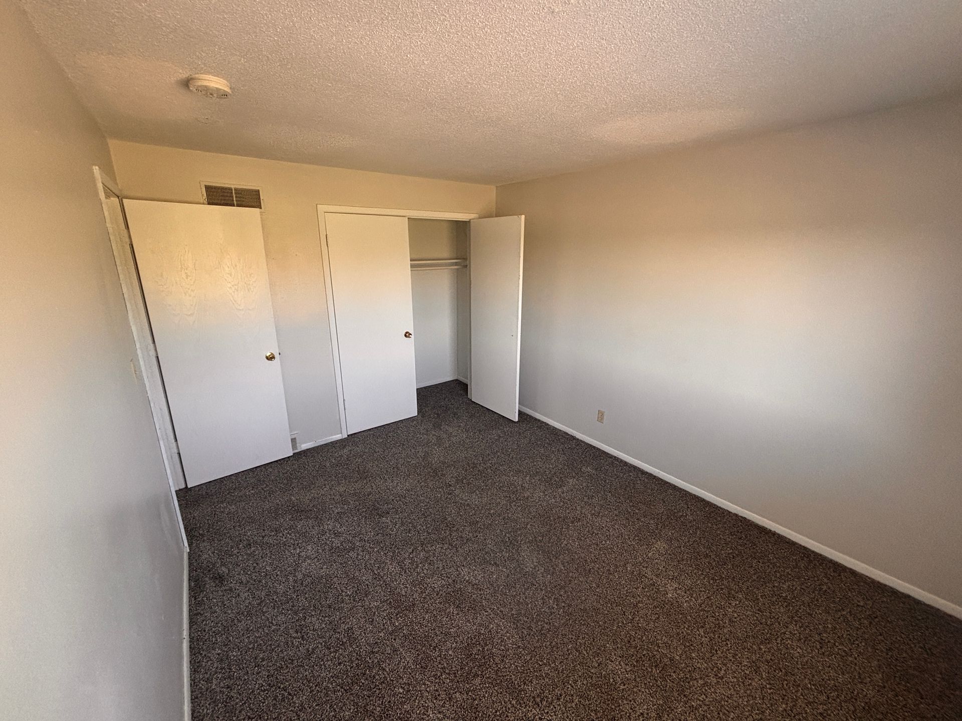 Empty beige bedroom with dark carpet, closet doors, and open closet space