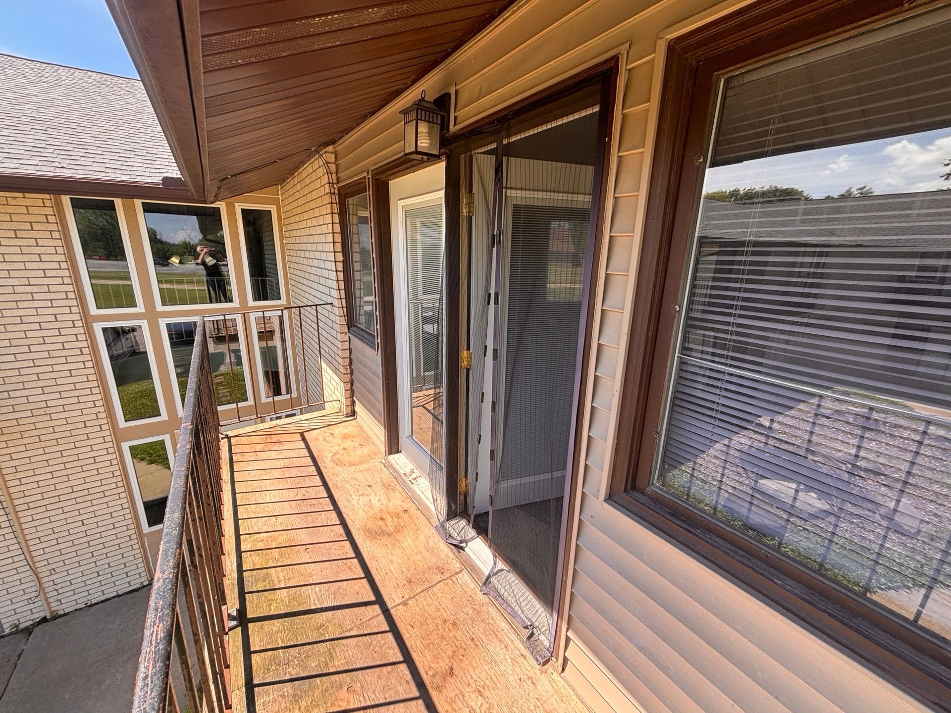 Sunlit apartment balcony with tiled floor, sliding glass doors, and a view of neighboring buildings