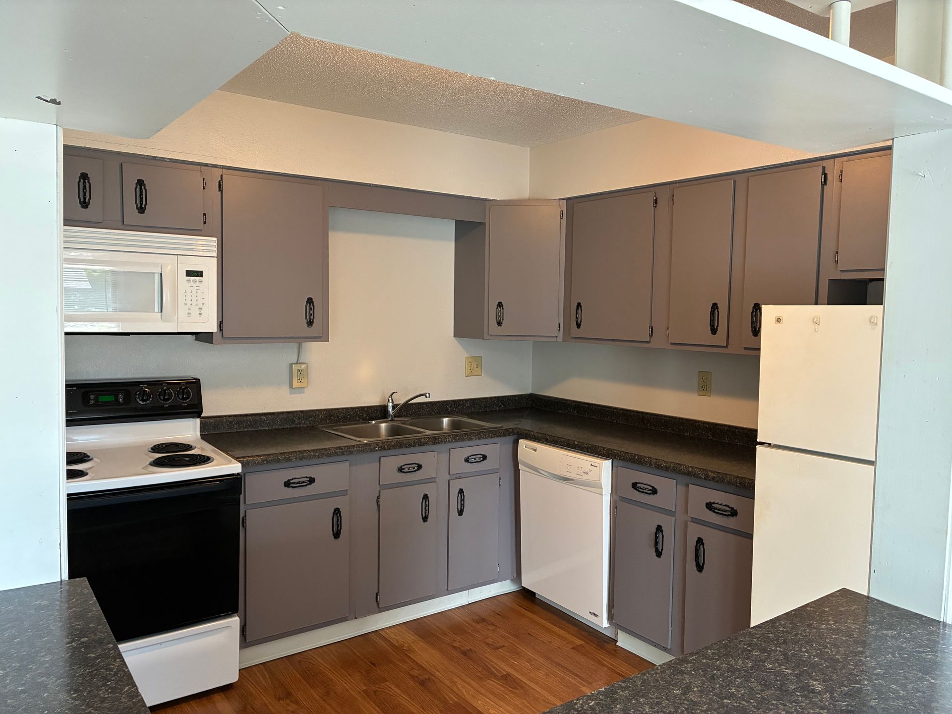 Compact kitchen with gray cabinets, black countertops, white appliances, and wood floor.