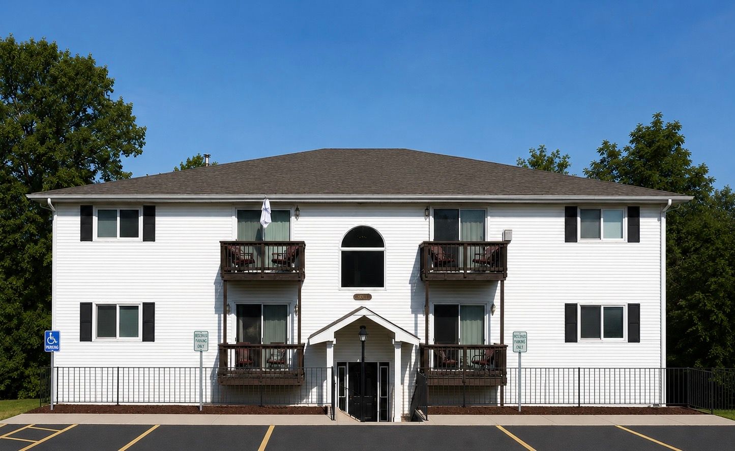 Two-story white apartment building with balconies, a central entrance, and a clear blue sky
