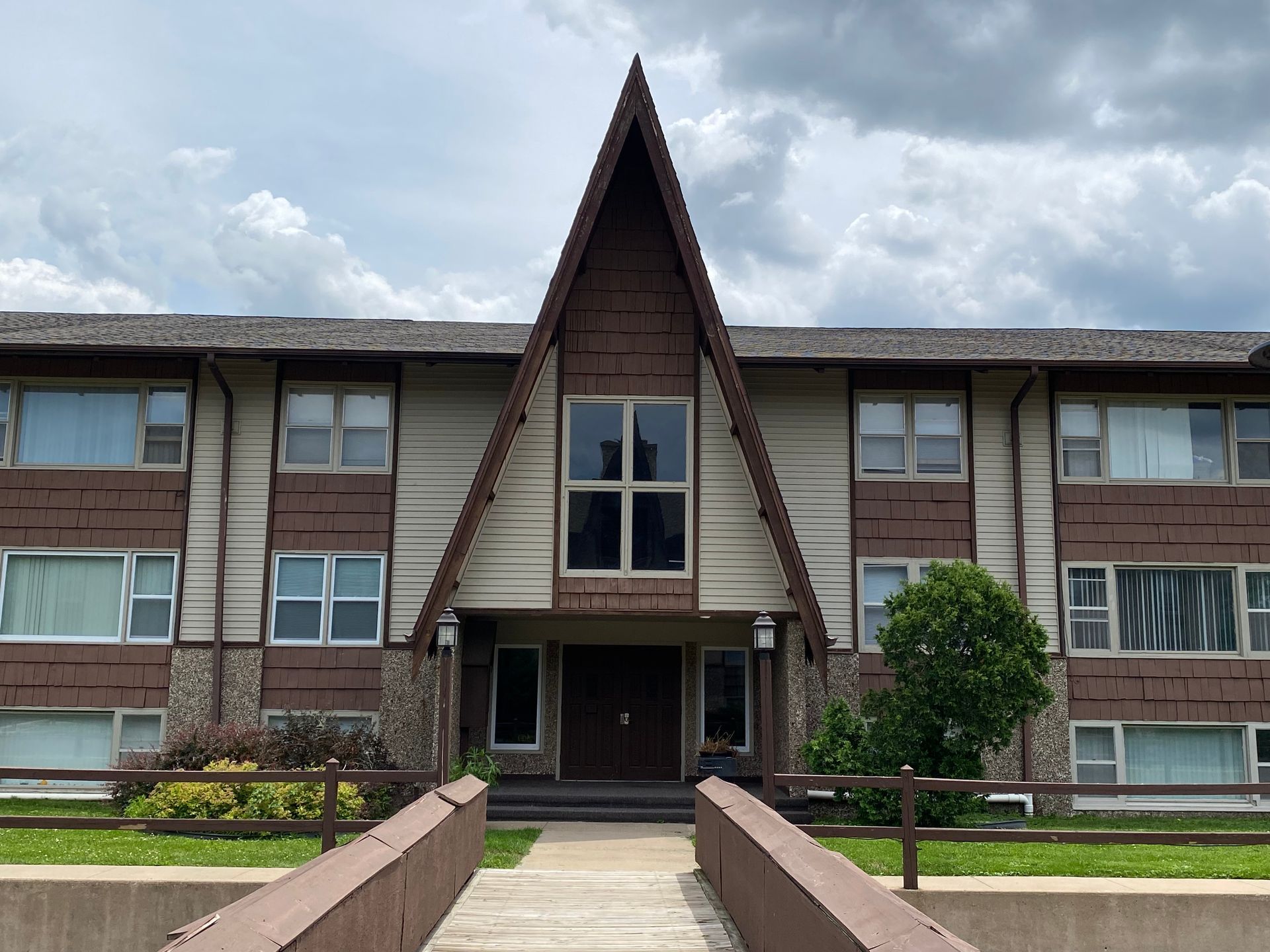 Apartment building with a steep triangular entrance, brown siding, and a central walkway