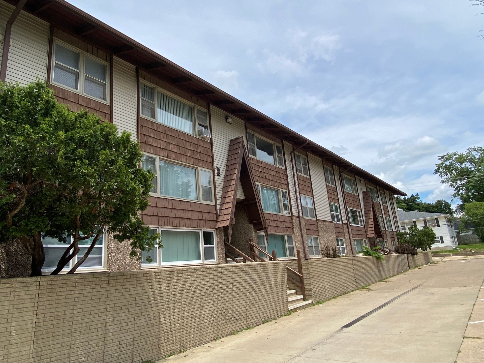 Brick apartment building along a paved walkway under a partly cloudy sky